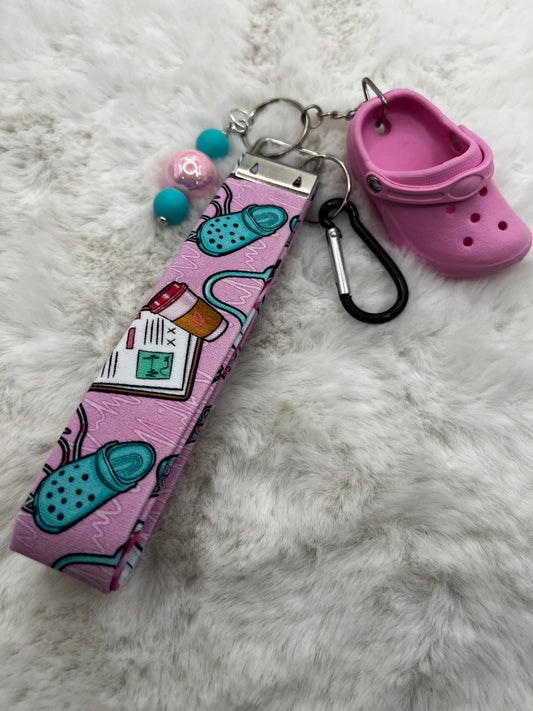 Keychain with pink lanyard strap featuring cartoon croc-themed drawings with a mini croc shoe charm on a white fluffy surface