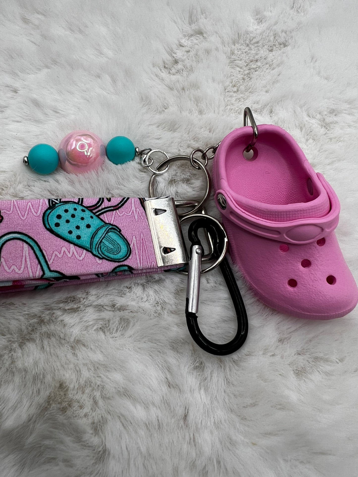 Pink lanyard keychain with croc shoe charm and beads on a fluffy white surface