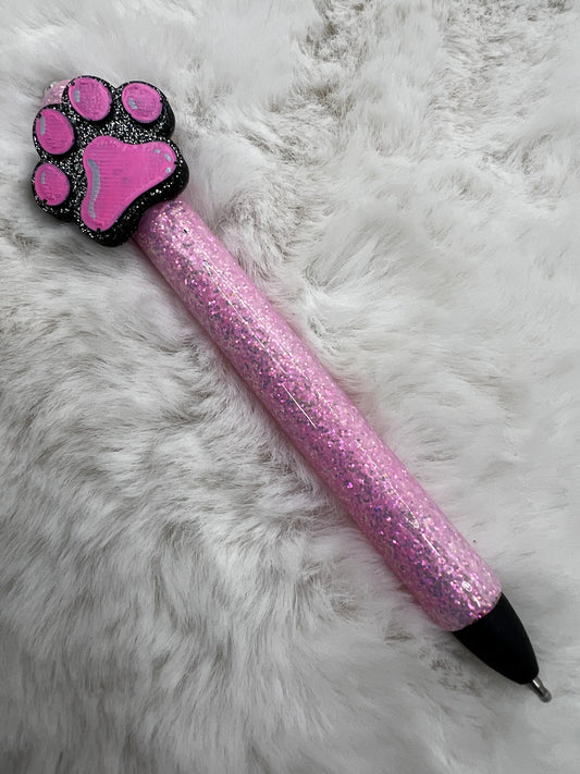 Pink glitter pen with paw-shaped top on a fluffy white surface