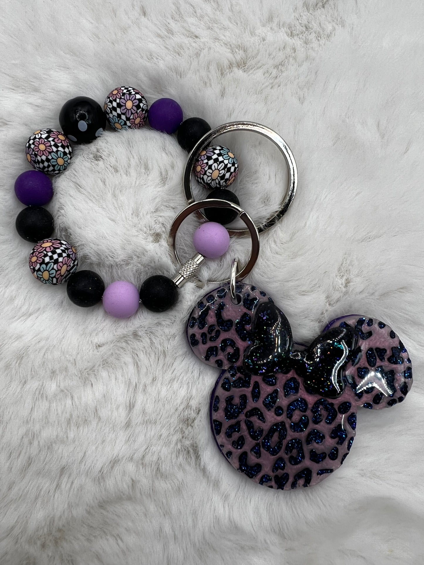 Bracelet with purple and black beads and a keychain with a leopard print Minnie Mouse design on a white fur background
