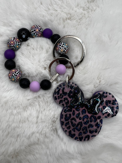 Bracelet with purple and black beads and a keychain with a leopard print Minnie Mouse design on a white fur background