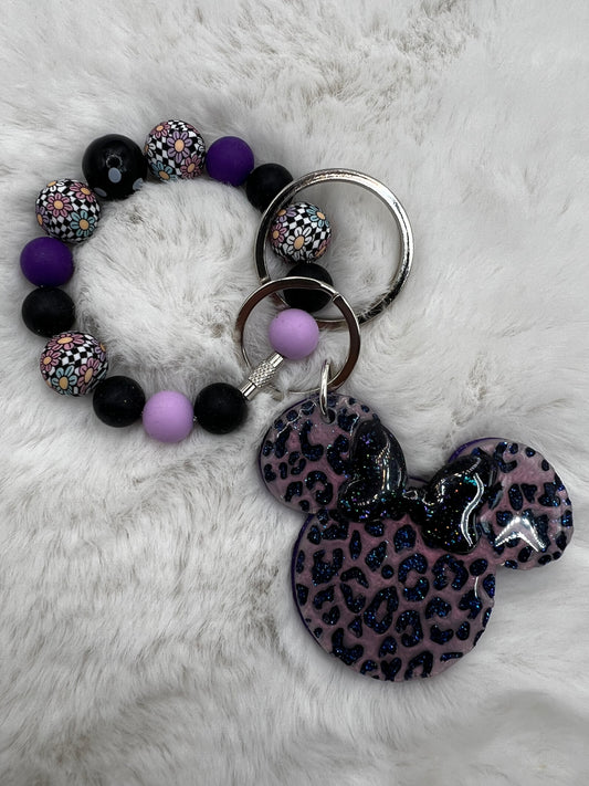 Bracelet with purple and black beads and a keychain with a leopard print Minnie Mouse design on a white fur background