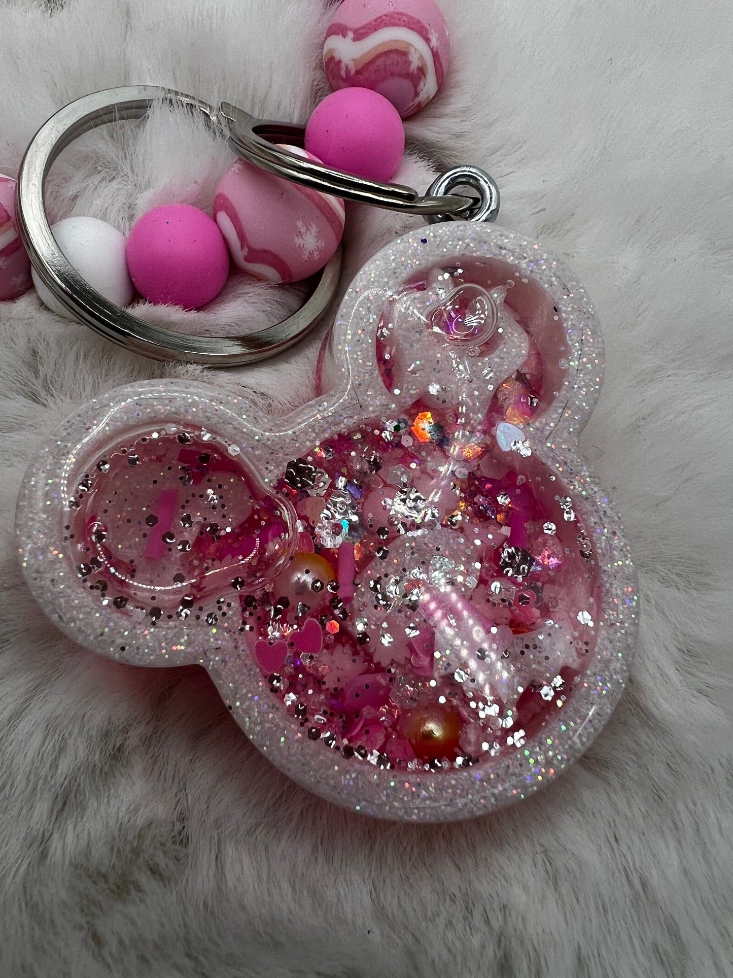 Pink glittery Minnie Mouse keychain with decorative elements on a fluffy white background
