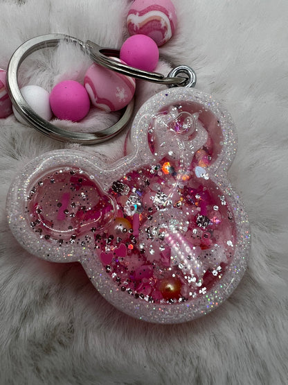 Pink glittery Minnie Mouse keychain with decorative elements on a fluffy white background