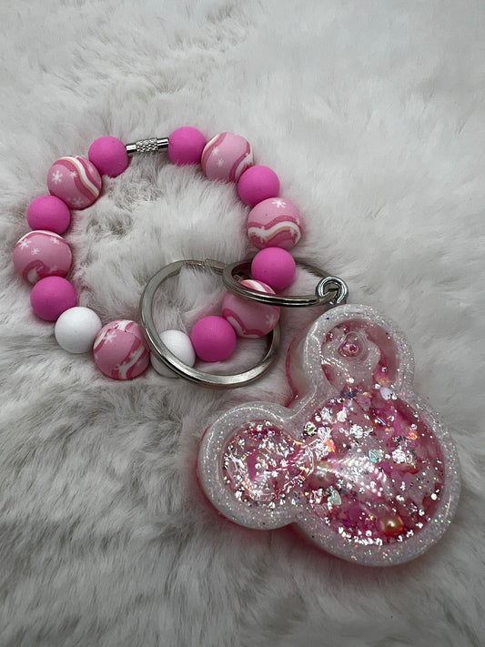 Pink and white beaded keychain with a glittery Minnie Mouse charm on a fluffy white background