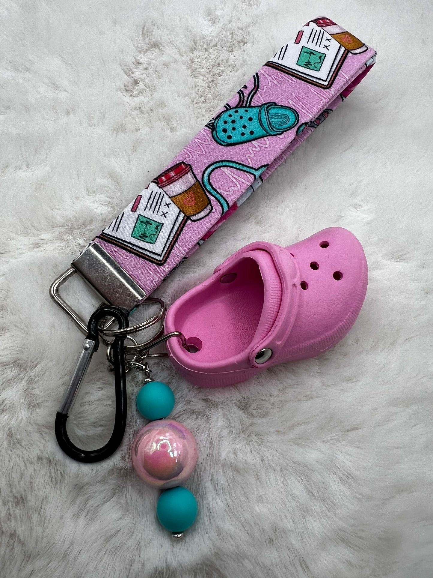 Pink croc shoe lanyard keychain with colorful beads and a lanyard on a white fur background