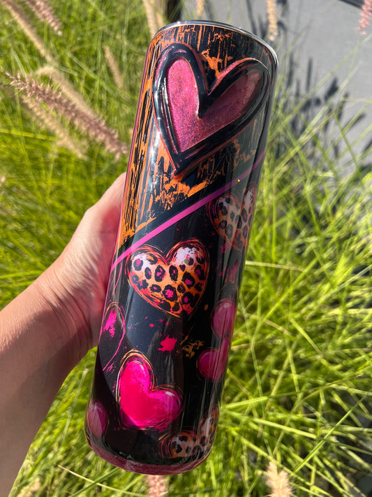 Hand holding a colorful tumbler with heart designs against a grassy background