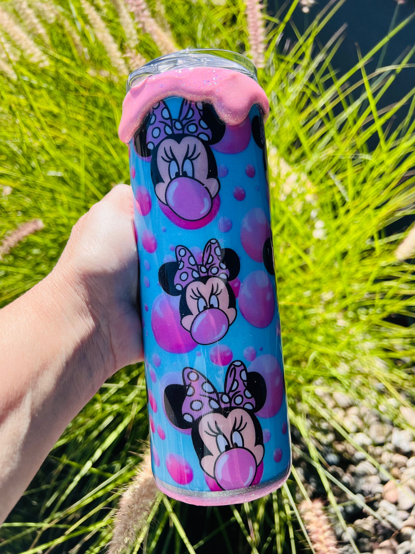 Sparkly pink and purple Minnie Mouse themed tumbler held in front of a grassy background