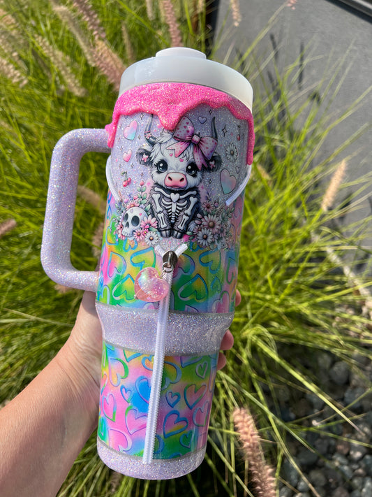 Colorful tumbler with cartoon cow design held by a hand against a natural background