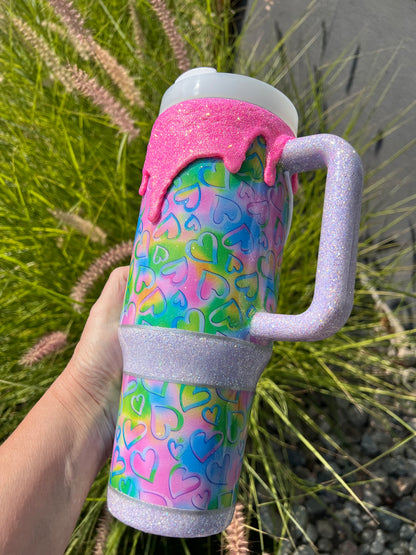 Colorful tumbler with heart pattern held by a hand against a natural background