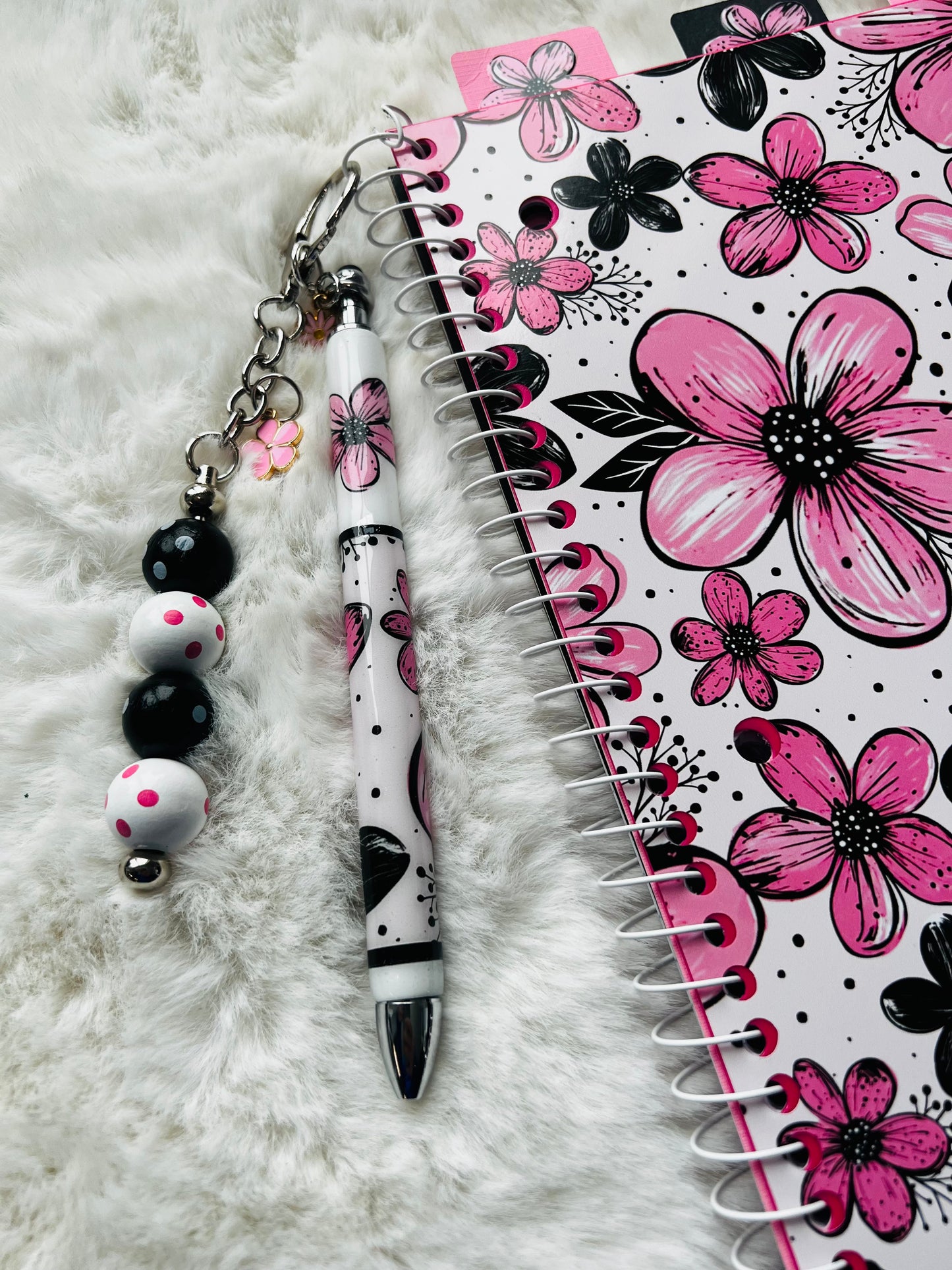 Pen with decorative keychain and floral notebook on a white surface