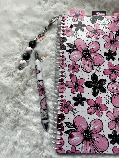 Notebook with floral design on cover, pen, and keychain on fluffy white surface