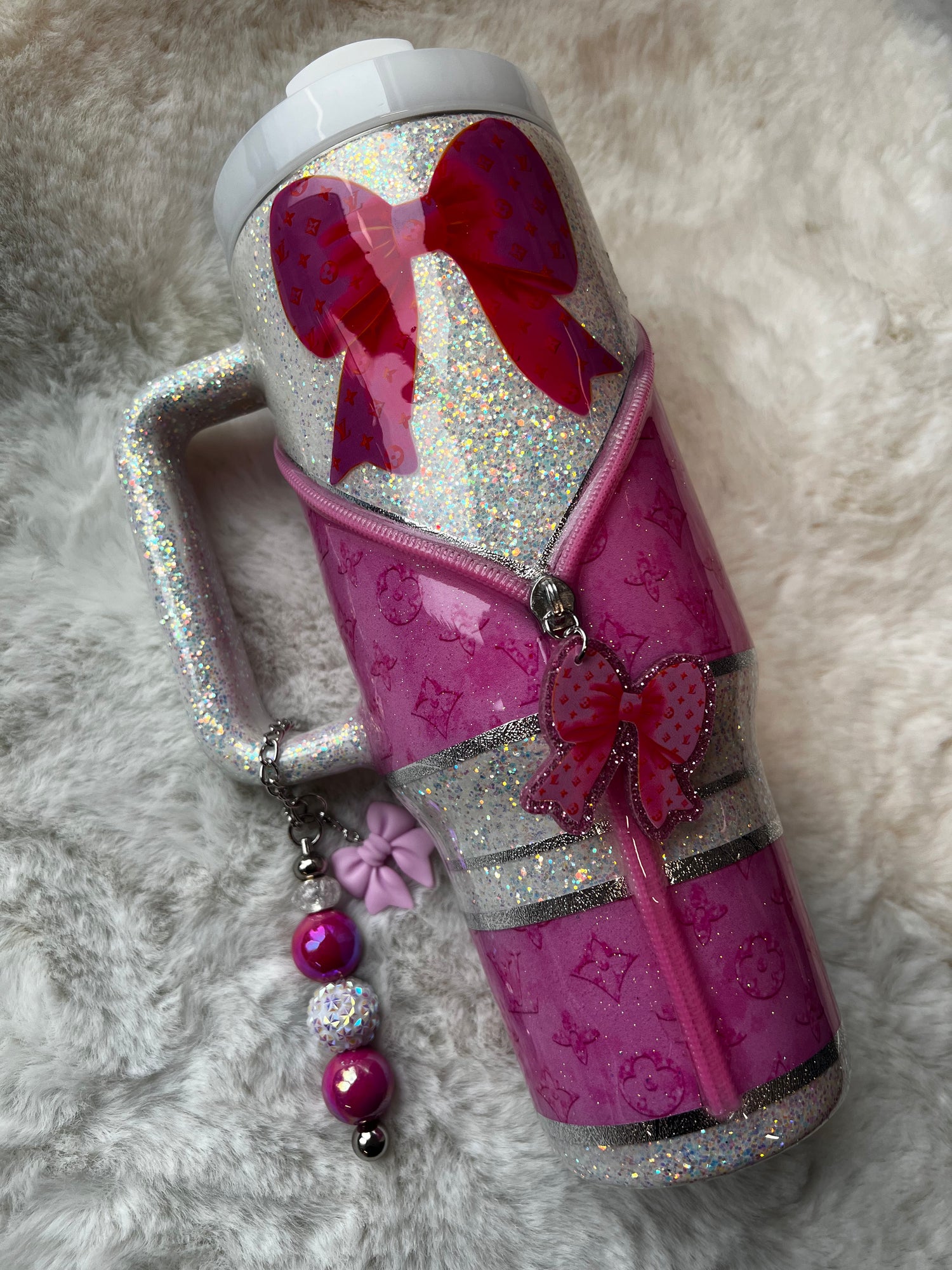 Pink sparkly tumbler with bow details and charms set on a fluffy surface