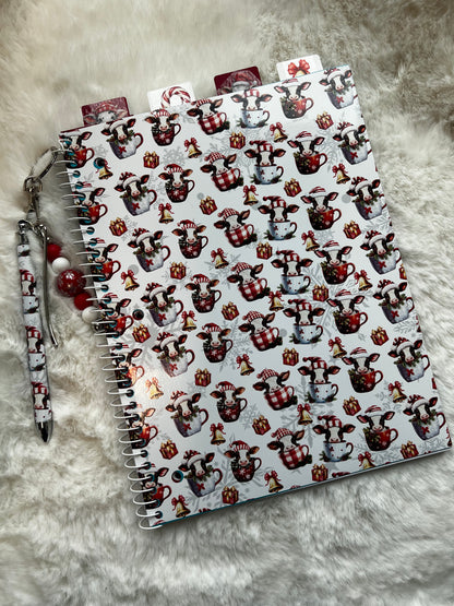 Notebook with cow pattern on cover and pen on gray surface