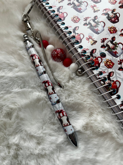 Decorative pen with cow design on a notebook with Christmas-themed stickers.
