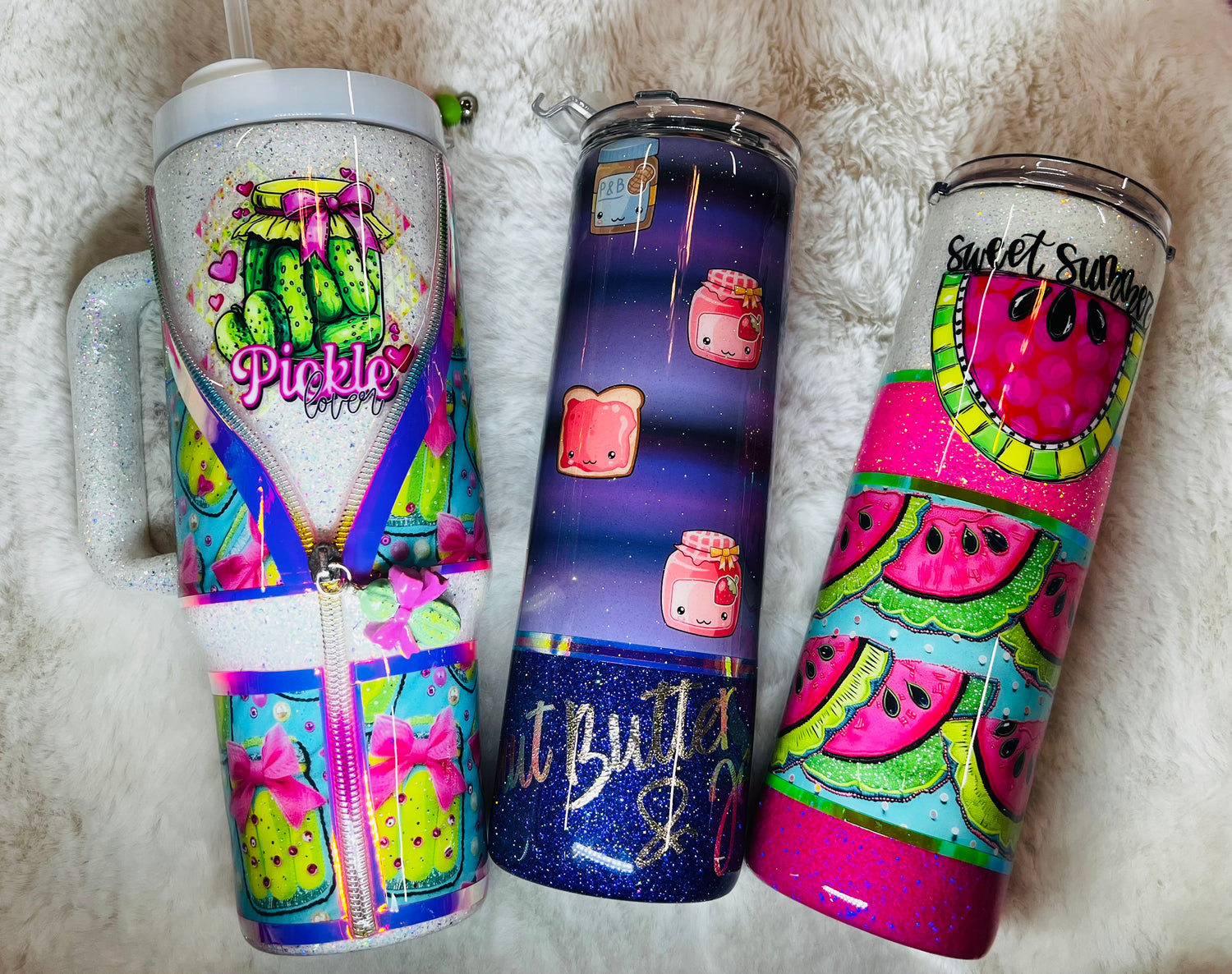 Three colorful custom tumblers by Tater T Co with various designs on a fluffy white surface